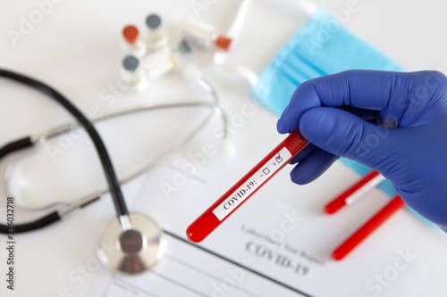 Coronavirus blood test concept. Doctor's hand in a medical glove holding a test tube with positive coronavirus blood over a laboratory desk. Coronavirus COVID-19. Pandemic.