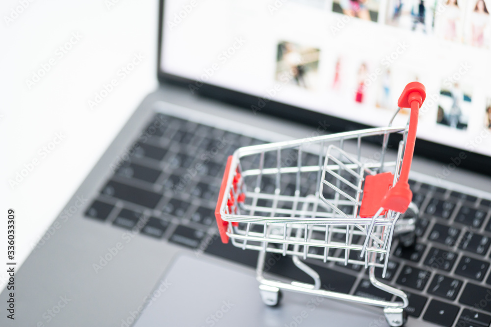 Red trolley on laptop keyboard.A cart and notebook computer on white background.Electronic commerce that allows consumers to directly buy goods from a seller over the internet.Shopping online concept.