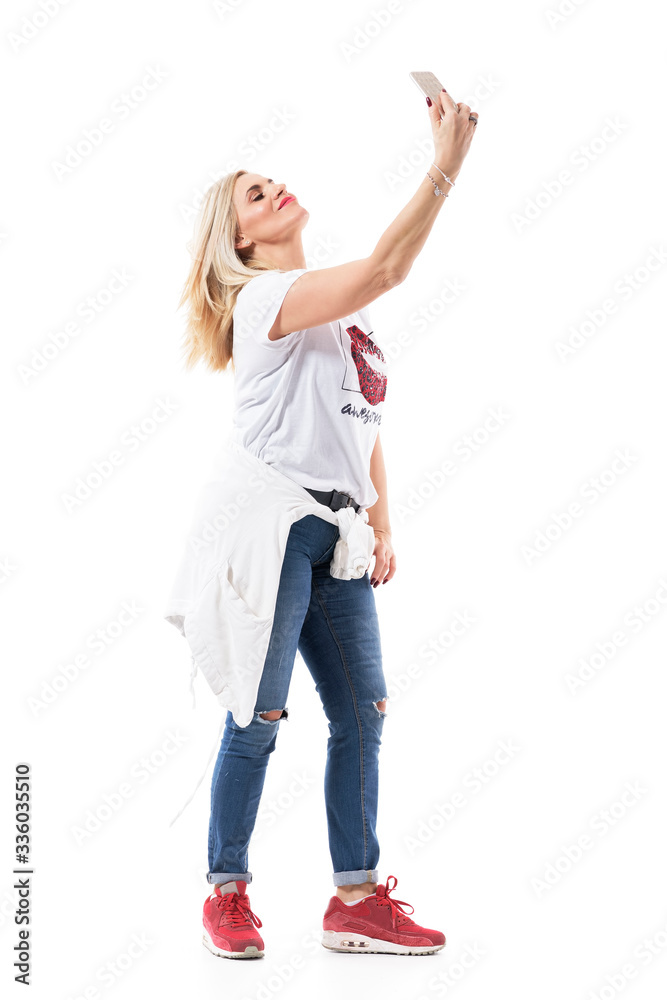 Carefree confident mid age beautiful woman posing and taking selfie photos with cellphone. Full body length isolated on white background. Carefree confident mid age beautiful woman posing and taking selfie photos with cellphone. Full body length isolated on white background.
