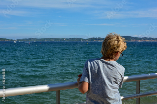 Boy stands on the railing, looking out over the sea to Saint-Tropez