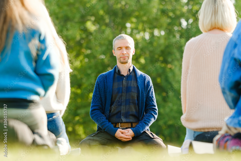 A group of young people meditate outdoors in a park. 
