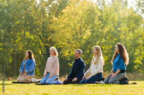 A group of young people meditate outdoors in a park. 