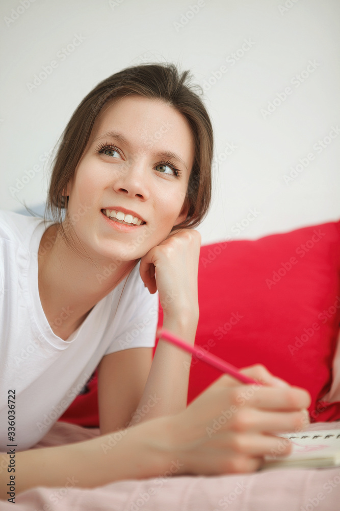 Young woman writing something in the notebook on the bed. Peaceful atmosphere. Woman stay home during a quarantine Young woman writing something in the notebook on the bed. Peaceful atmosphere. Woman stay home during a quarantine