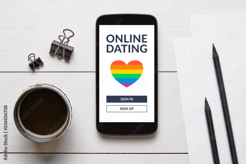 LGBT dating app concept on smart phone screen with office objects on white wooden table. Gay online dating. Top view