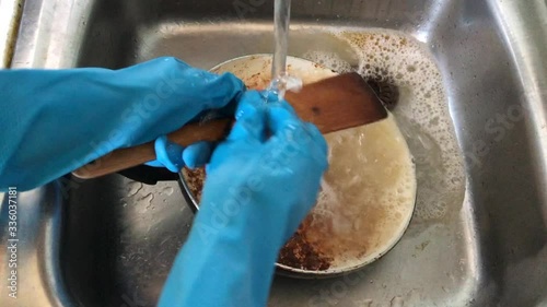 A woman in rubber gloves washes dirty dishes in the sink with a sponge with foam. Washing dirty dishes at home in the kitchen.