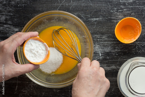 Fototapet Top view of woman hands putting starch into yolks and sugar in bowl for making c