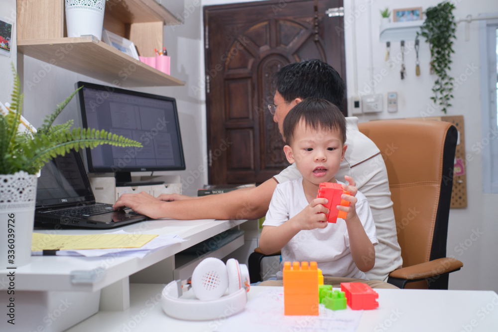 Asian kindergarten boy having fun playing blocks near his working at home father, while in quarantine isolation during the Covid-19 health crisis Asian kindergarten boy having fun playing blocks near his working at home father, while in quarantine isolation during the Covid-19 health crisis