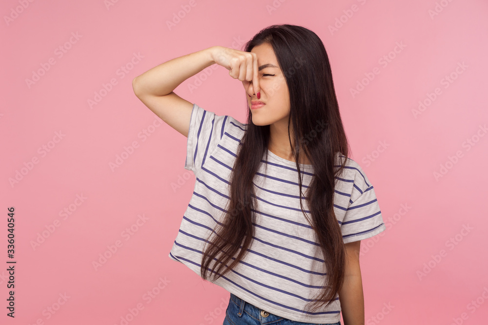 Smells bad! Portrait of confused girl with brunette hair in t-shirt pinching her nose to hold breath, feeling repulsion and disgust to unpleasant odor. indoor studio shot isolated on pink background Smells bad! Portrait of confused girl with brunette hair in t-shirt pinching her nose to hold breath, feeling repulsion and disgust to unpleasant odor. indoor studio shot isolated on pink background