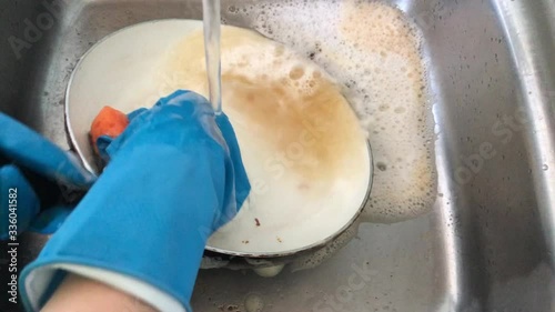 A woman in rubber gloves washes a dirty pan with a foam sponge in the sink. Washing dishes at home in the kitchen.