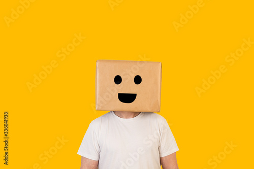 Hombre con caja de cartón en la cabeza con una sonrisa en la cara sobre fondo amarillo liso brillante. Vista de frente. Copy space photo