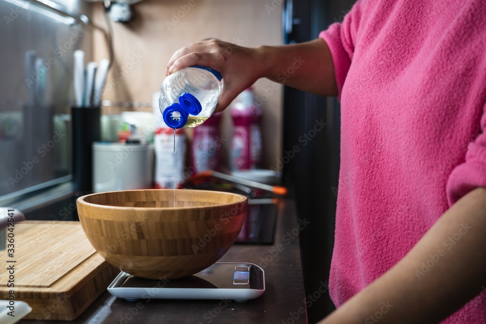 Fototapeta Woman in a pink sweater pouring oil into a wooden bowl