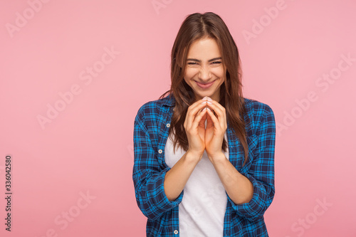 Portrait of sneaky scheming young woman in checkered shirt thinking devious plan with cunning evil face expression, having slyly idea to prank friend. indoor studio shot isolated on pink background