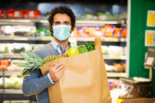 Masked man holding an healthy food bag in supermarket during the coronavirus pandemic photo