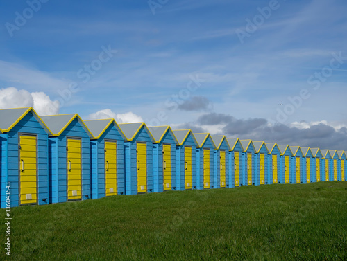 Colourful line of beach huts with grass and blue sky. No people.