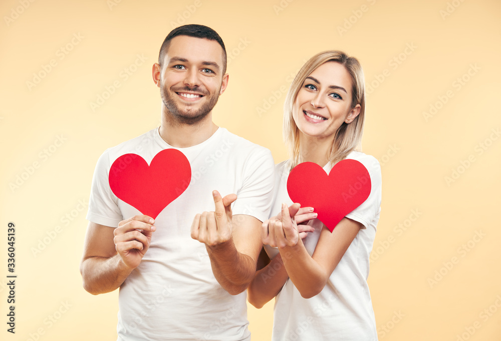 Young couple in love holding big paper hearts in hands over studio background Young couple in love holding big paper hearts in hands over studio background