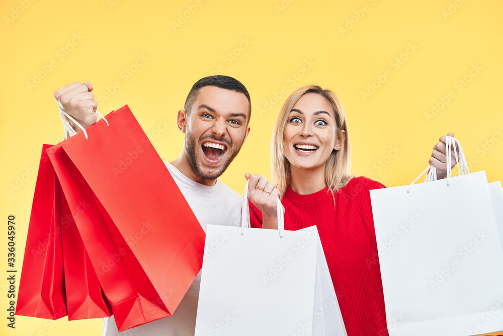 Young happy couple holding shopping bags in hands isolated over yellow background Young happy couple holding shopping bags in hands isolated over yellow background