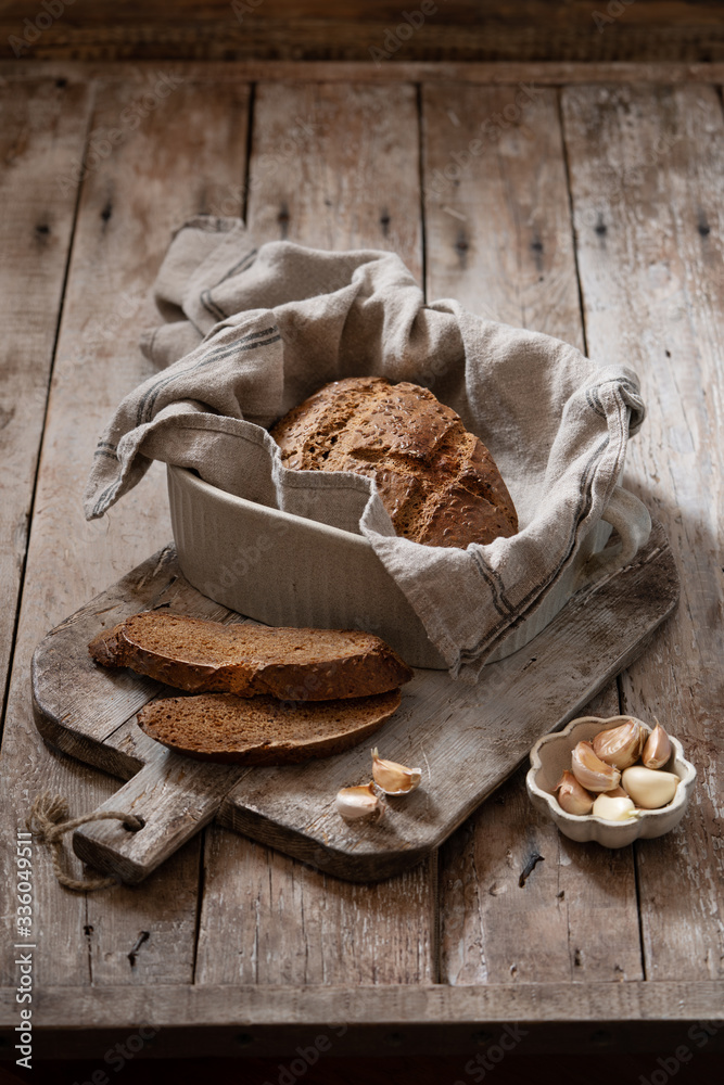 Latvian sweet and sour bread with sesame seeds and garlic. Freshly baked traditional wholegrain bread in textile napkin in ceramic baking form. Copy space, vertical banner. Atmospheric food  image