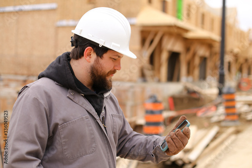 Caucasian architect browsing by smartphone at construction site.