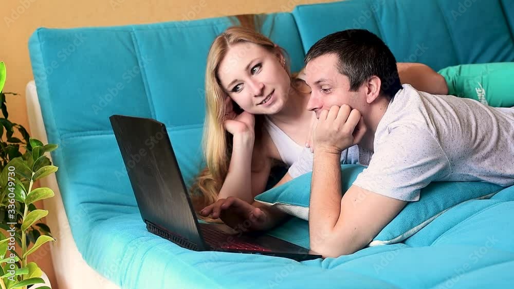 a man and a girl are lying on the couch and looking at a laptop, stay at home. home insulation, protection from covid-19 coronavirus. minimalistic living room interior. happy couple and time. a man and a girl are lying on the couch and looking at a laptop, stay at home. home insulation, protection from covid-19 coronavirus. minimalistic living room interior. happy couple and time.