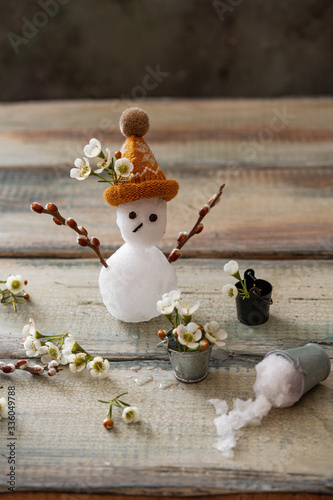 the spring equinox or hello spring concept. Funny card with broken snowman and melted snow in buckets. Flowers and snow on the scales. Copy space for text