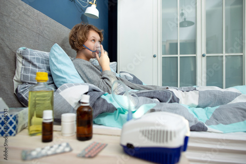 Portrait of a young woman doing inhalation at home. Use nebulizer and inhaler for the treatment. Young woman inhaling through inhaler mask.