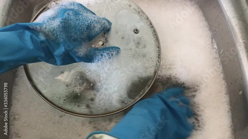 A woman in rubber gloves washes dirty dishes in the sink with a sponge with foam. Washing dirty dishes at home in the kitchen.