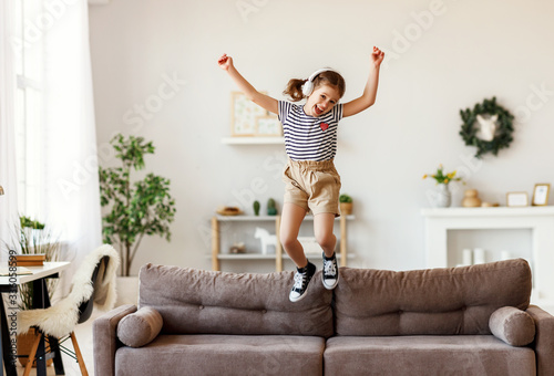 Fototapeta Naklejka Na Ścianę i Meble -  Happy girl listening to music and jumping on sofa.