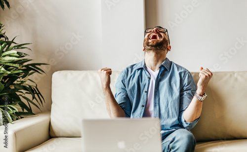 Excited male businessman celebrating victory, success, triumph  while working at laptop photo