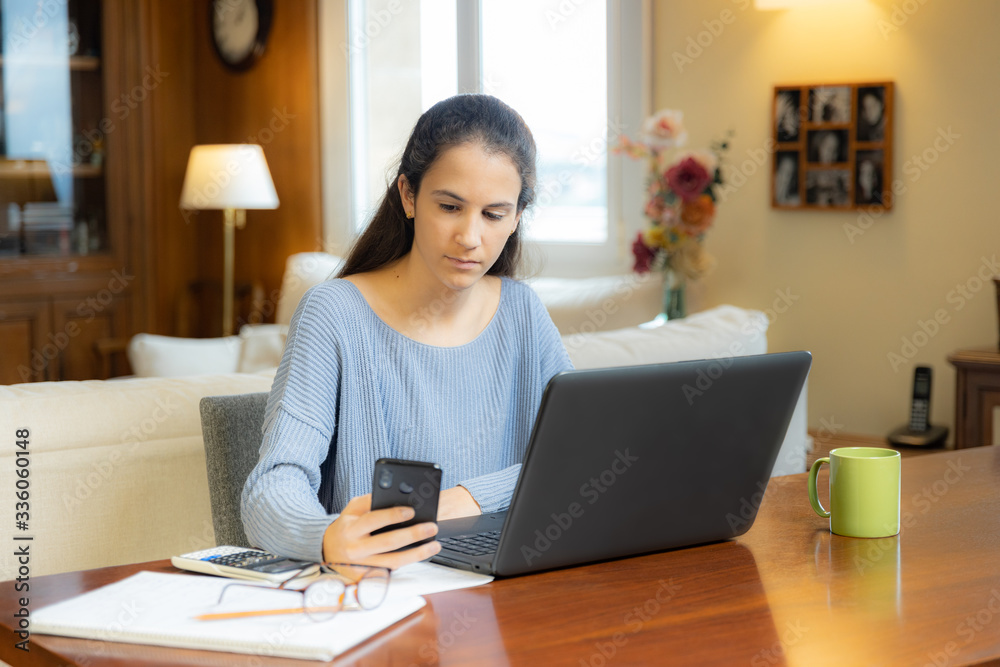 Young student girl looking at smartphone with laptop at home Young student girl looking at smartphone with laptop at home