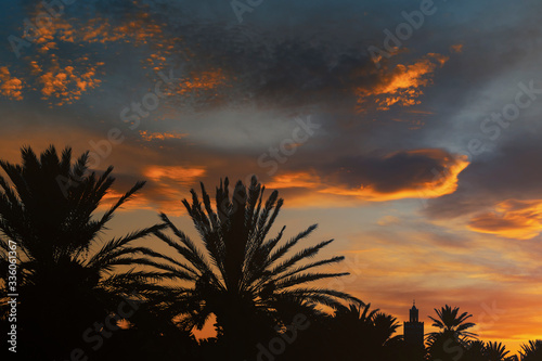 Silhouette of a minaret  mosque  and date palms against a beautiful colorful sky at sunset.