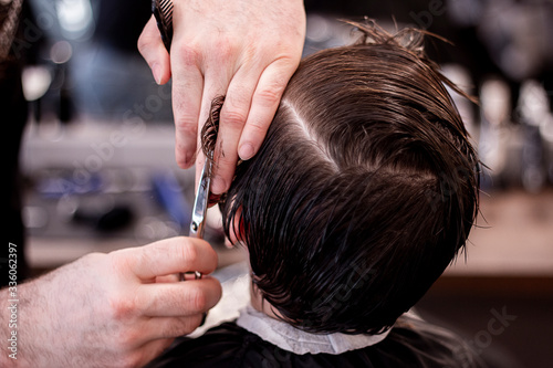 Barber cutting little boys hair with scissors. Little boy in barbershop.  © Natia