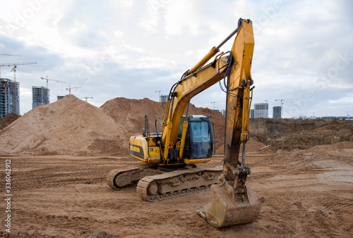 Yellow excavator during earthworks at construction site. Backhoe digging the ground for the foundation and for laying sewer pipes district heating. Earth-moving heavy equipment