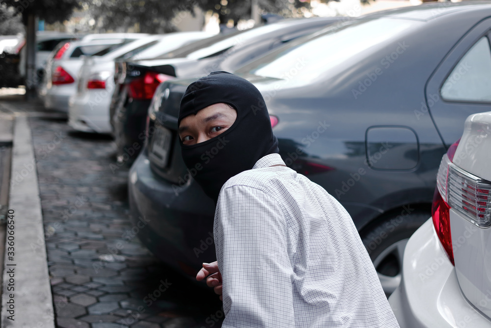 Masked thief in black balaclava trying to break into car. Criminal crime concept.