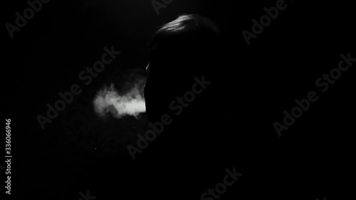 the silhouette of a man on a dark background exhales clouds of smoke