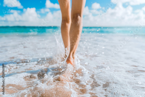 Legs of a beautiful young girl who runs towards the ocean on a sandy beach. Vacation on the Paradise beaches of Asia. Summer and vacation holiday concept. Ocean foam wraps around the girl's legs. Phot