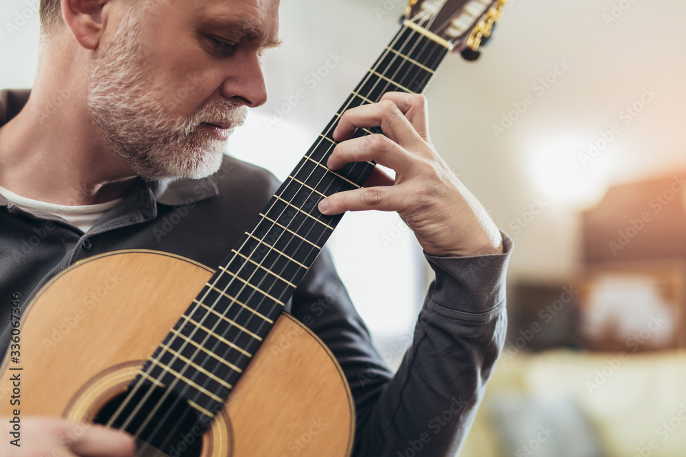 Obraz premium Handsome mature man in casual clothes is smiling while playing guitar at home