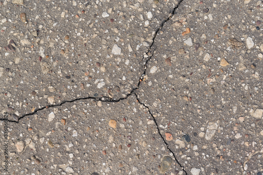 Obraz premium The surface of the asphalt with a triple crack. The asphalt is rough with protruding stones of different sizes, shapes and colors.Texture, background, backdrop.