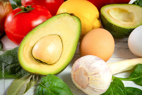 half an avocado with a stone,  tomatoes,  lemon, spinach, eggs, garlic on a white background,   close up, healthy food,