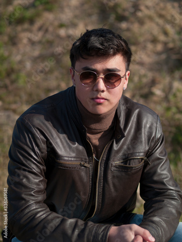 junger Mann in Lederjacke und Sonnenbrille sitzt draußen