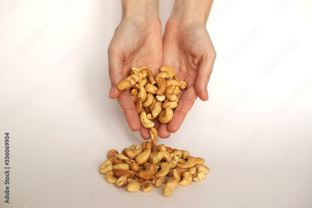 Female hands sprinkle nuts on a white isolate. Girl's hands pour cashew nuts on a white background. Female hands sprinkle nuts on a white isolate. Girl's hands pour cashew nuts on a white background.