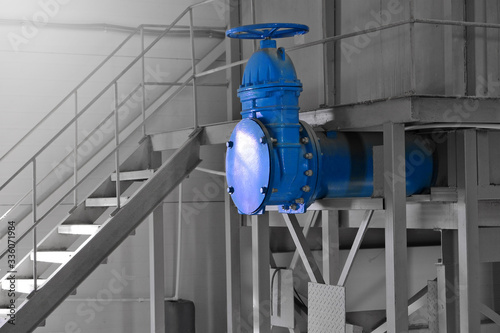 big blue dead end water pipe with tap or valve or faucet on gray industrial background with metal stairway