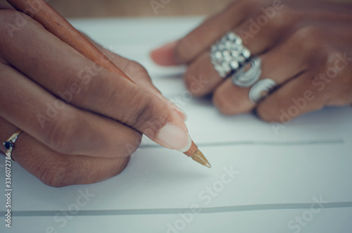 Closeup of the hands of a black woman filling a paper document.  Selective focus on her right index finger.   photo