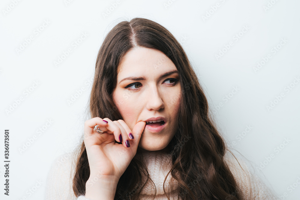 brunette girl bites his nails on a white background brunette girl bites his nails on a white background