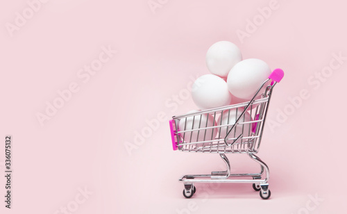 shopping cart full of easter eggs on pink background. Creative Easter concept.