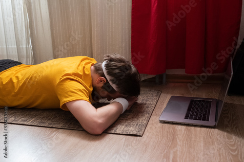Young man meditating on a floor and lying in Makarasana pose at his living room