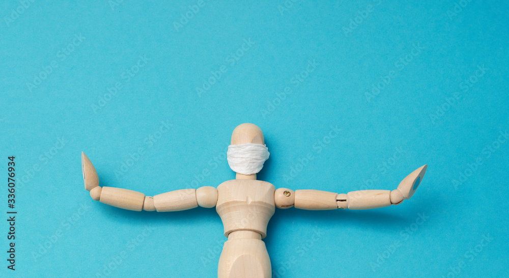One wooden man mannequin in a protective medical mask holds his hands in different directions lies sick on a blue background. Concept - keep your distance during quarantine. One wooden man mannequin in a protective medical mask holds his hands in different directions lies sick on a blue background. Concept - keep your distance during quarantine.