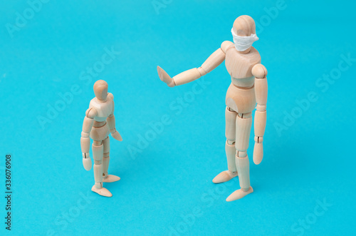 Concept - take care of the health of loved ones  keep your distance during quarantine. One wooden man mannequin in protective medical mask holds hands in front of him refusing contact with small child