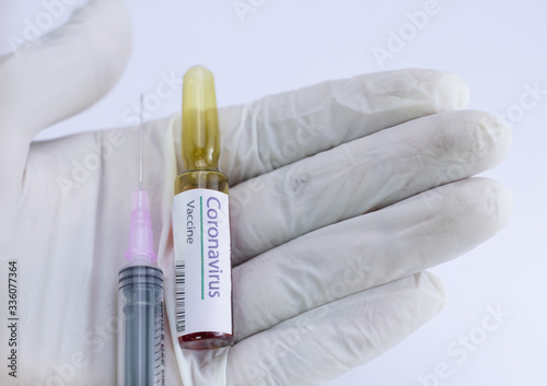 Coronavirus vaccine ampoule with an injection held in the palm covered by surgical glove.