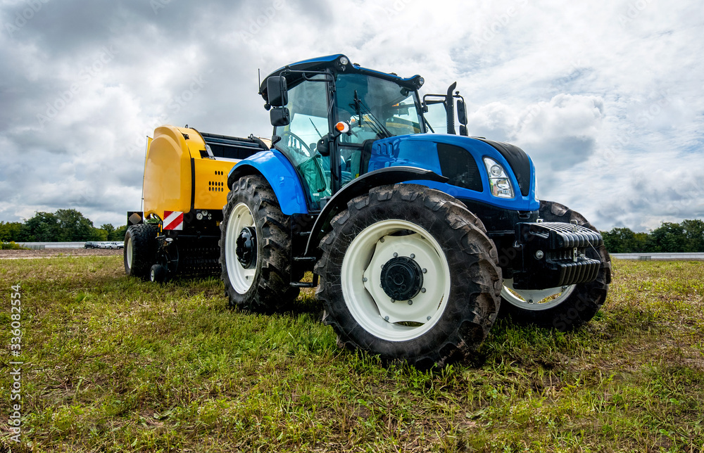 Obraz premium new blue tractor with baler in motion at field at agro exhibition at summer time