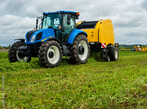 new blue tractor with baler in motion on farmland with cloudy sky